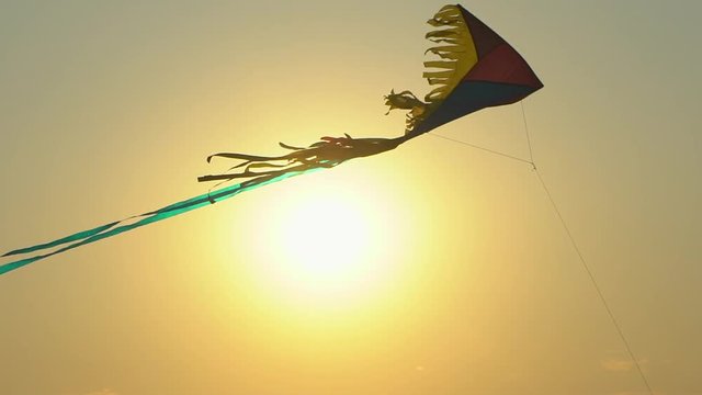 Close up toy kite flying high air in the wind against gold sunset sky background sun lens flare. Colorful kite flying in sunny summer sky. Toy children fun leisure activity recreation happy holiday