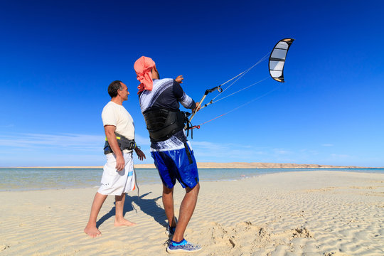 Two men on sea shore sand beach learning to pilot training kite in blue sky with wind, recreation leisure vacation fun active hobby. Sunny summer warm day. Kite boarding water sports lessons course