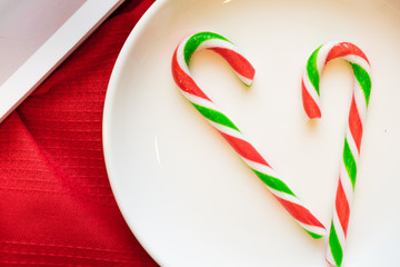Christmas decoration. Candy on the white plate over red background with light. Candy cane. 