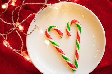 Christmas decoration. Candy on the white plate over red background with light. Candy cane. 