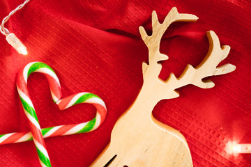 Christmas decoration. Wood Deer play toy and Candy over red background with light. Candy cane. 