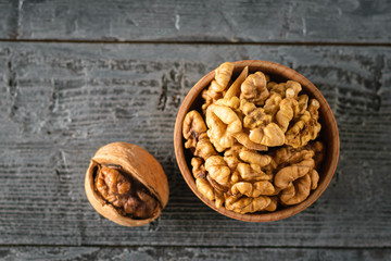 One split walnut and a clay bowl with walnut kernels on a dark wooden table. The view from the top.