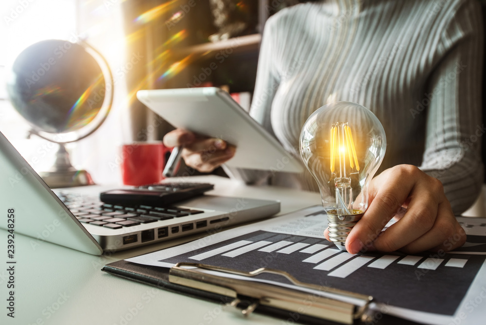 Poster business hand holding lightbulb with using laptop computer and money stack in office. idea saving en