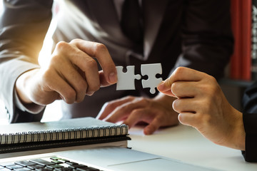 Business solutions and success concept. Businessman hand connecting jigsaw puzzle at office in morning light