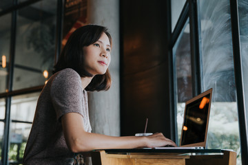 Beautiful young Asian woman working at a coffee shop with a laptop.