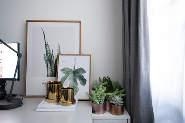 Composition of gold mirror ceramic pots with artificial plants inside setting on minimal books and...