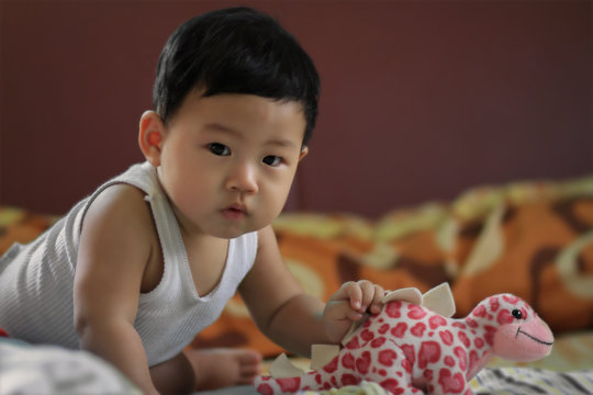 under 1 year old cute Asia baby boy sit on the bed in a cozy room with his toy and sunset light, Processed photo in soft focus and selective at face, Background for kindergarten or nursery