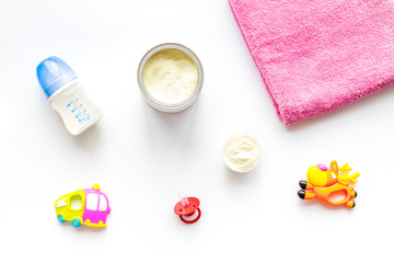 Toys for newborn baby set with plastic rattle and milk in bottle on white background flat lay