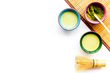 Japanese matcha tea ceremony concept. Matcha powder, ready matcha tea, accessories on bamboo table mat on white background top view copy space