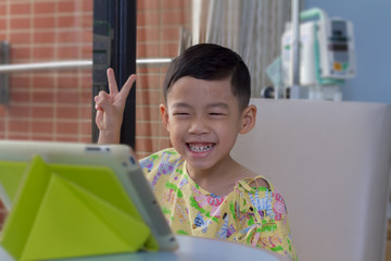 Allergy sickness Asian black hair boy with happiness and big smile background. Alone 4 year old patient kid in hospital room using tablet video call to school and talking with his teacher and friends