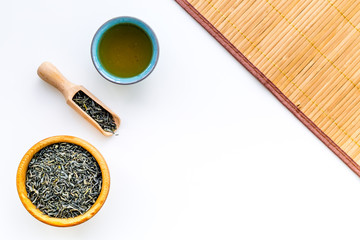 Chinese tea concept. Tea ceremony. Dry tea leaves in bowl and wooden scoop near cup of tea on white background and bamboo table mat top view copy space