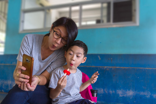 Mom And Son Selfie With Mobile Phone Background. Asian Black Hair 40s Woman And 4 Years Old Boy Happiness To Using Smartphone Taking Photos Or Video With Selective Focus And Copy Space