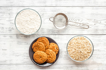 Cook cookies at home concept. Ingredients and instruments for make cookies. Fresh cookies near flour and sieve on white wooden background top view