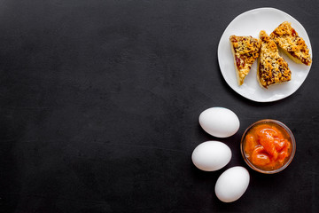 Ingredients for homemade cookies. Fresh cookies near jam, eggs on black background top view copy space