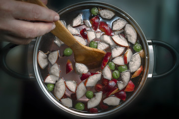 Woman Stirs Colorful Apple Slices, Gooseberries, Fruit Mix in a Pot With a Wooden Spoon on a Stove.  Refreshing Fruit Apple Cider Punch Party Drink.