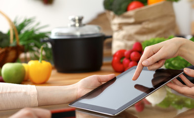Close-up of human hands using tablet or touch pad. Two women in kitchen. Cooking, friendship or online shopping concepts
