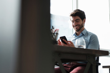 Man in Office Smiles After Sending Message Using Smartphone