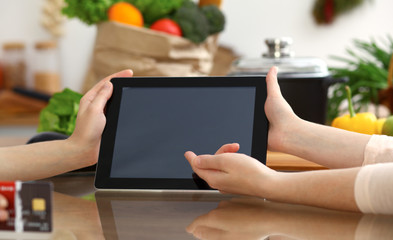 Close-up of human hands using tablet or touch pad. Two women in kitchen. Cooking, friendship or online shopping concepts