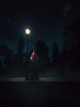 dramatic lit image of a clown besides a lamp post at night