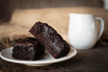 Brownie cake placed on a white plate with a glass of white milk placed beside it. Putting on a wooden desk