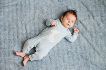 Newborn pretty baby boy in blue sleepwear lying on grey sheet, top view