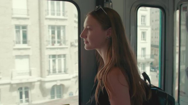 Side view of a woman looking out at the city lost in thought as she rides a train in Paris in the summertime