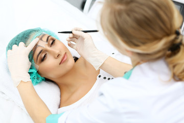 Naklejka premium Professional beautician is going to correct eyebrow line at woman face using cosmetic ruler. Permanent brow makeup in beauty salon, closeup. Cosmetology treatment