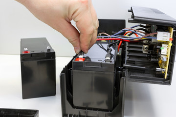 Male hand connects 12 volt battery in uninterruptible power supply. Repair and maintenance of UPS. Replacing battery. - obrazy, fototapety, plakaty