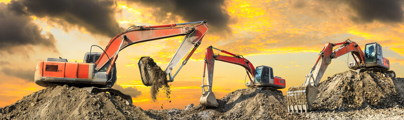 Three excavators work on construction site at sunset,panoramic view