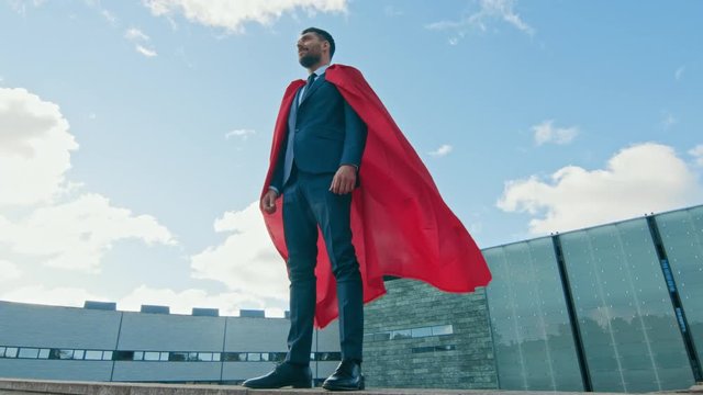 Businessman Superhero WIth Red Cape Blowing in the Wind Stands on the Roof of a Skyscraper Ready to Make Business Transactions and Save the Day. Low Angle Shot.