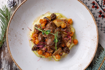 Appetizing meat with tender mashed potatoes, taiga cloudberry berries and pickled cedar cones. View from above. Dish with original serving.