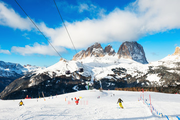 Skiers skiing down the slope in ski resort in winter Dolomites. Val Di Fassa, Italy.
