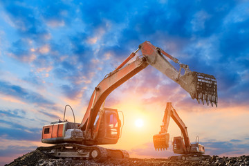 Two excavators work on construction site at sunset