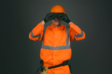 Geodesist or builder foreman is looking through a binoculars in his hands isolated on gray...
