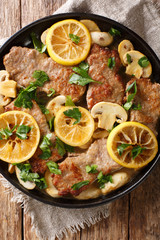 Italian veal scaloppini with mushrooms and lemons in a sauce close-up in a frying pan. Vertical top view