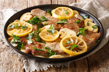 Scaloppini tender veal cooked with mushrooms and lemons in a spicy sauce close-up in a frying pan...