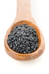 Heap of black organic beluga lentils in wooden spoon on white
