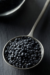 Heap of black organic beluga lentils in metal spoon on black stone