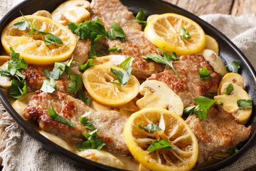 Scaloppini veal cooked with mushrooms and lemons in a spicy sauce close-up in a frying pan. Horizontal