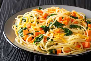 Low-calorie lunch of spaghetti with pumpkin, spinach and cheddar cheese close-up on a plate. horizontal