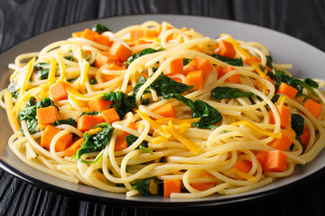 Healthy autumn meal of spaghetti with pumpkin, spinach and cheddar cheese close-up on a plate on the table. horizontal