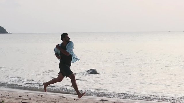 Cinematic footage. Young handsome man is running at the beach at sunset time.