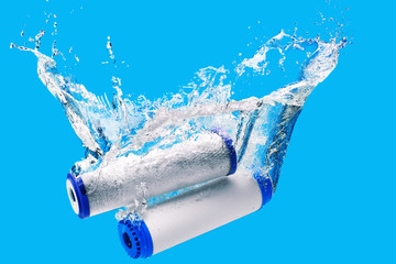 New carbon filter cartridge for house water filtration system isolated on blue background. Splash....