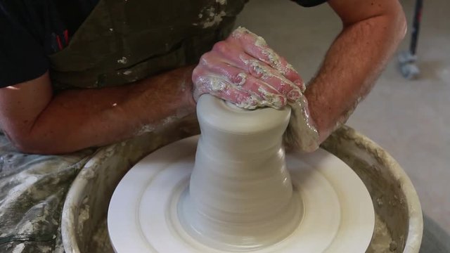 Potter creating a ceramics clay vase. Man sculptor in the workshop makes a jug out of earthenware closeup. Twisted potter's wheel. Hands detail. Small business concept.