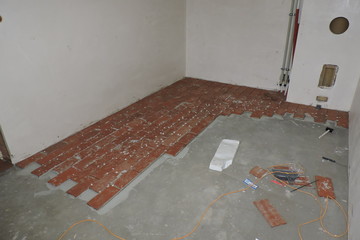 Laying floor tiles in a boiler room under construction and a knife, a rubber hammer, polystyrene foam and a dustpan on the concrete floor - obrazy, fototapety, plakaty