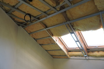 A room with a metal frame of a ceiling under construction insulated with mineral wool  - obrazy, fototapety, plakaty
