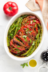 Baked whole pork meat with tomatoes, green beans and black olives, homemade cozy winter dish in a pot. Christmas tasty food