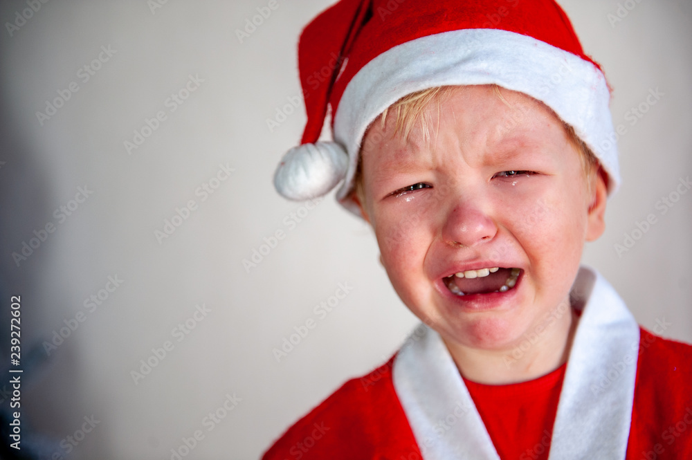 Wall mural funny child in santa claus costume is crying without christmas present. tradition of family holidays