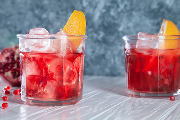 Fresh pomegranate cocktail with mint, orange and ice blue concrete background with ingridients. Red cocktail close up. Copy space for text, logo or brand.