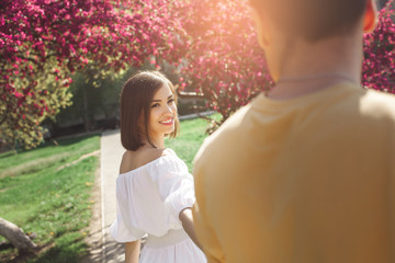 Fototapeta premium Attractive young people walking in park. Pretty couple together. Woman and man inlove. Girl taking her boyfriend by the hand outdoor